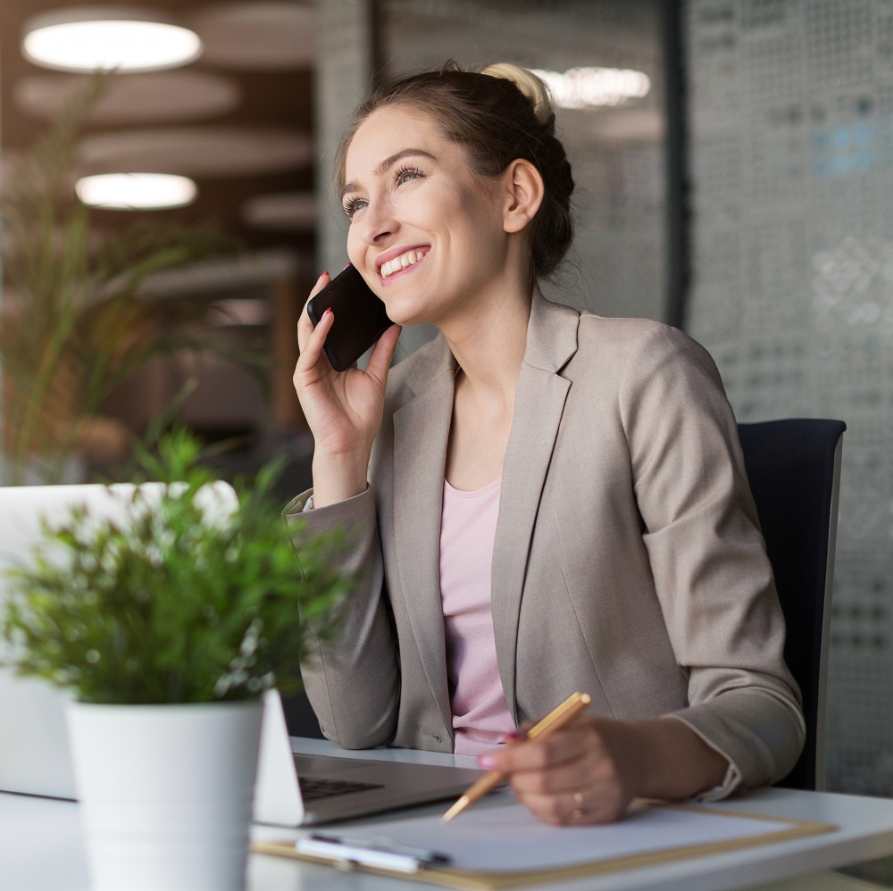 Webdesignerin sitzt im Büro für Webentwicklung am Schreibtisch und telefoniert mit Kunden über das Design der neuen Webseite