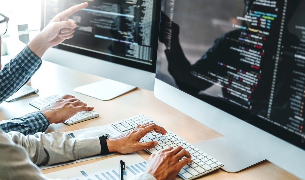 Zwei Webdesigner sitzen nebeneinander m Büro für Webentwicklung am Schreibtisch und besprechen die Webgestaltung des Kunden